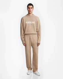 A person faces forward in the Rudsak GEIGER - 9524512 Camel M sweater and matching knit lounge pants with drawstring, paired with white sneakers, all set against a plain white background.