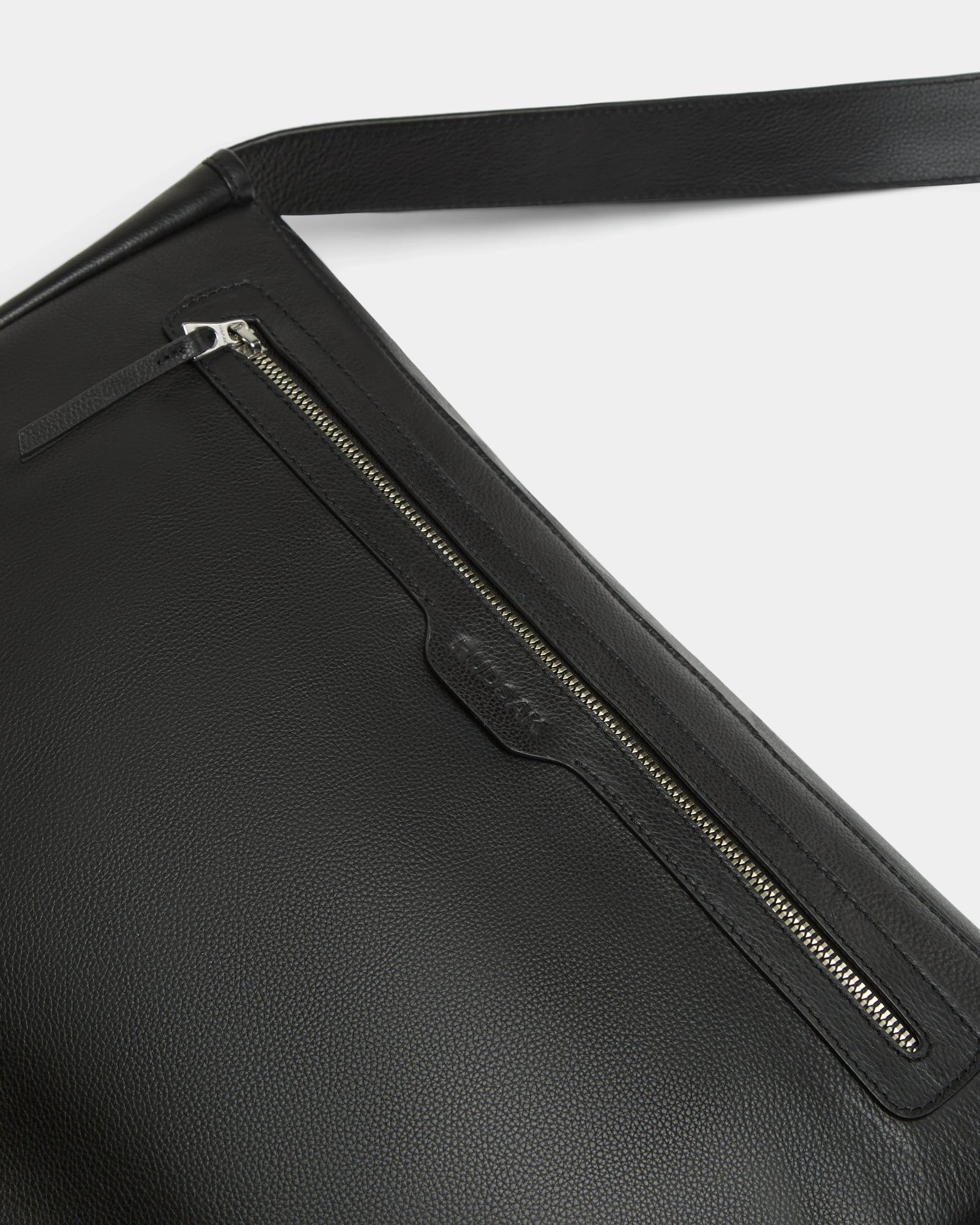 Close-up of the Rudsak GRAYSON L - 8324525 Black leather crossbody bag with a textured finish, silver zipper pocket, and matching leather pull tab. An adjustable strap is partly visible against a white background.