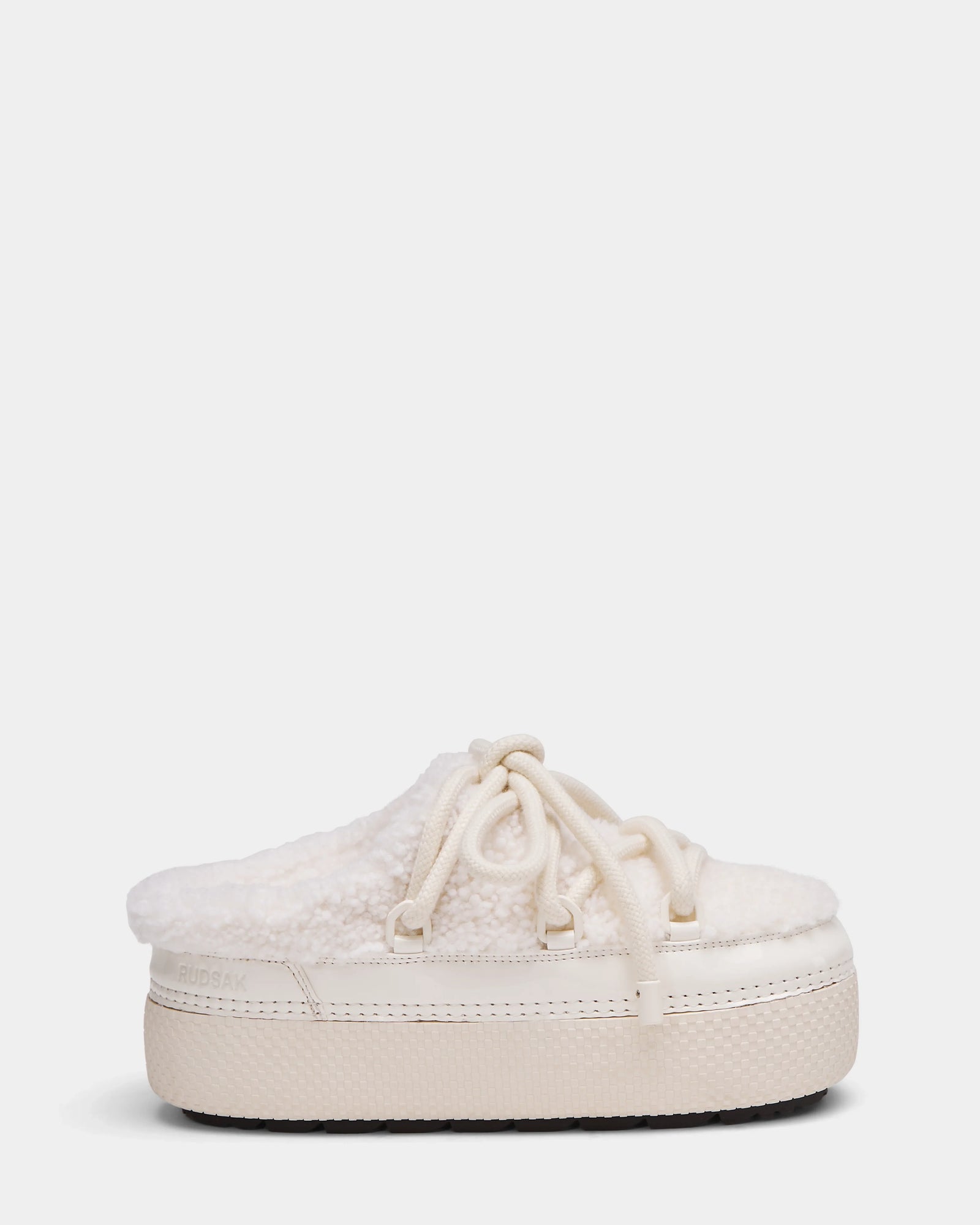 The Rudsak HARRIET - 8224519 Iceland is a cream women’s slipper mule featuring a thick rubber sole, faux shearling upper, lace-up detail, and cozy textured finish, shown from the side on a plain white background.