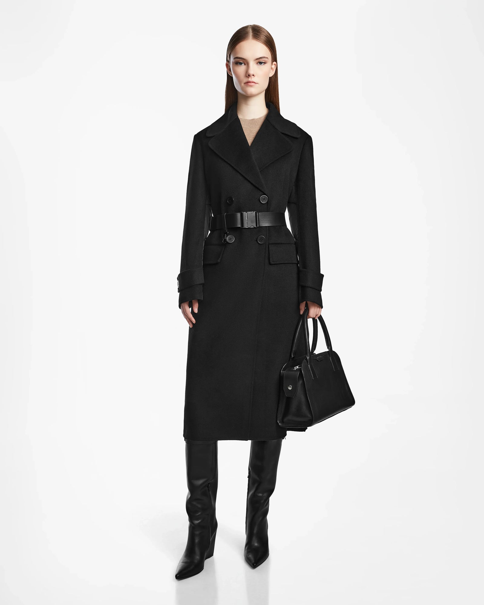 A woman with straight brown hair and a neutral expression stands against a white background, wearing the IVE - L124560 Black wool blend long coat by Rudsak, paired with black knee-high boots and a black handbag.