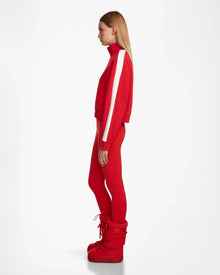 A woman stands in profile against a plain white background wearing the Rudsak KELLIE - 8524615 Flame Red top with white sleeve stripes and large red boots.
