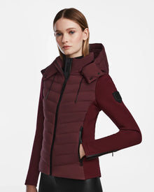 A woman wears the Rudsak MALYA M - L123547 Wine down quilted jacket with a hood, black zippers, and matching long sleeves, standing against a white background.