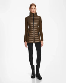 A woman faces forward wearing the Rudsak MARRY - L121003 Light Olive puffer coat with black sleeves, black leggings, and black ankle boots against a plain white background. The jacket features sleek waterproof zippers for style and function.