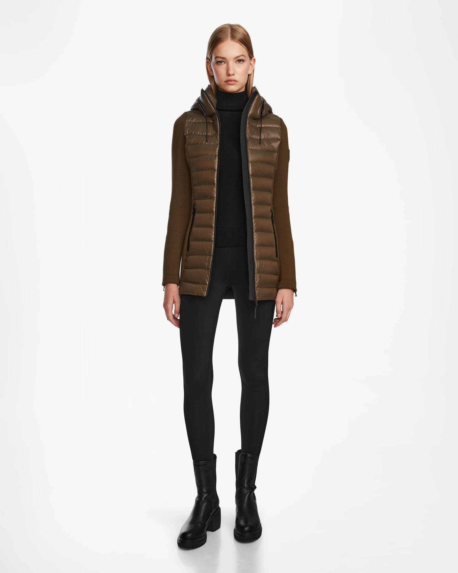 A woman faces forward, wearing the Rudsak MARRY - L121003 Light Olive womens puffer jacket with waterproof zippers over a black turtleneck, black leggings, and black ankle boots against a plain white background.