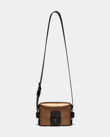 The Rudsak OFILIA - 8324504 is a compact, metallic antique bronze leather crossbody bag with a long adjustable black strap and front black buckle, shown on a plain light background.