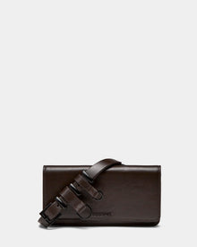The PREYA - 8324508 Espresso by Rudsak is a rectangular dark brown leather clutch with a wide matching shoulder strap and black metal buckles, displayed on a plain light gray background.