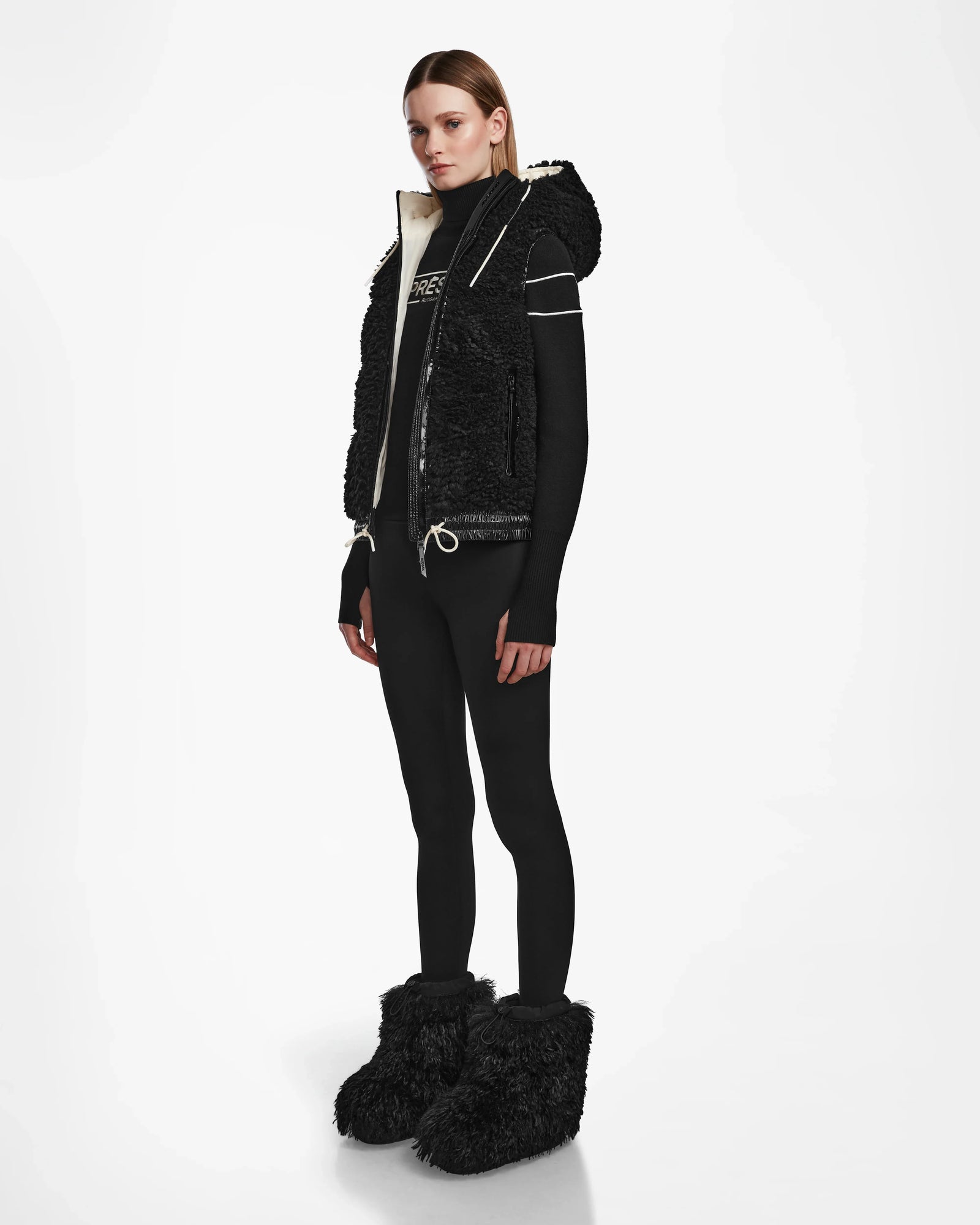 A woman in black clothing completes her look with the Rudsak RAQUEL S - 8124526 Black teddy ski vest, a cozy choice for winter mountain adventures.