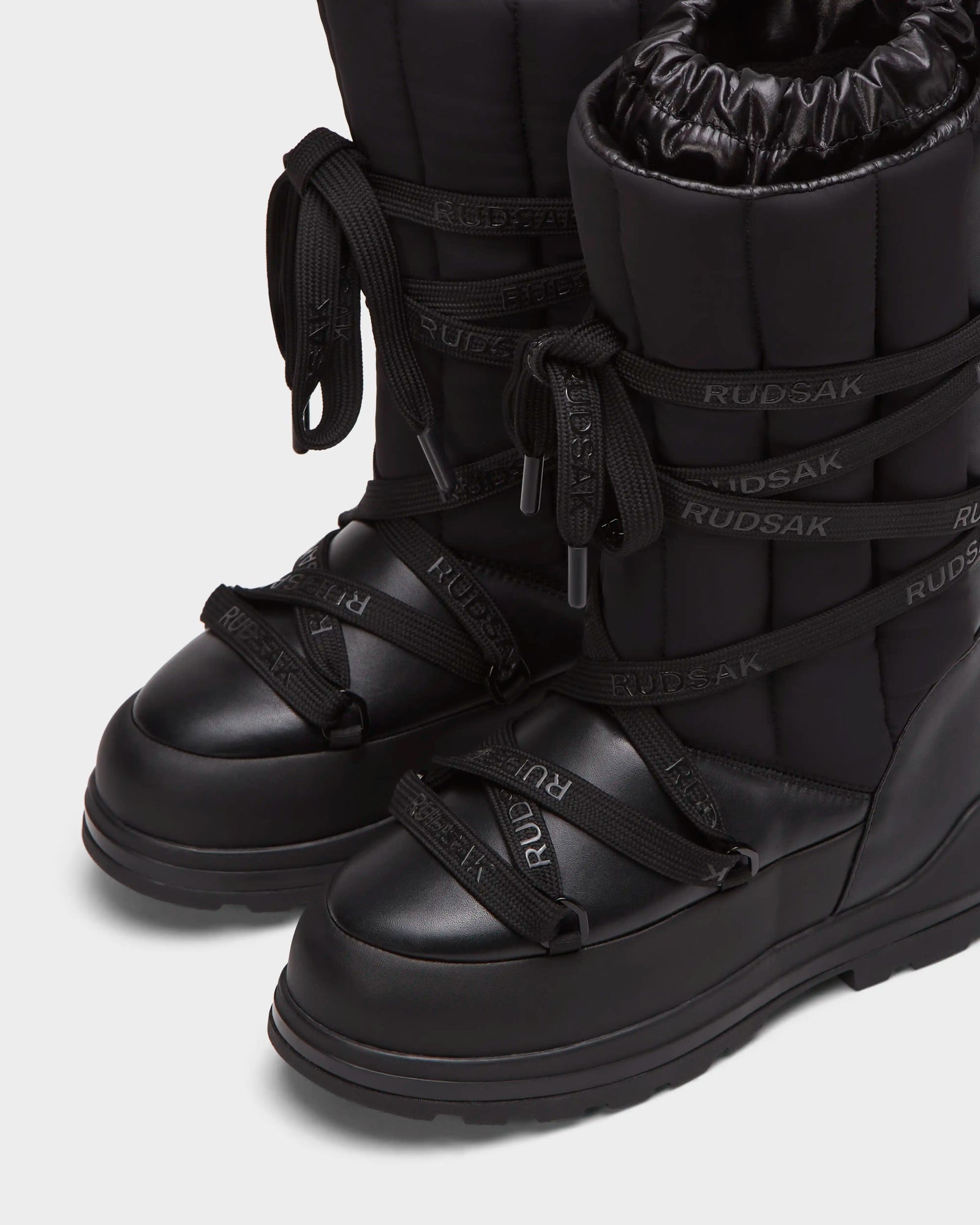 Close-up of RODIN - 8224502 Black womens winter boots by Rudsak, featuring thick anti-slip soles, padded quilted texture, high shaft for warmth, and crisscrossing branded laces.