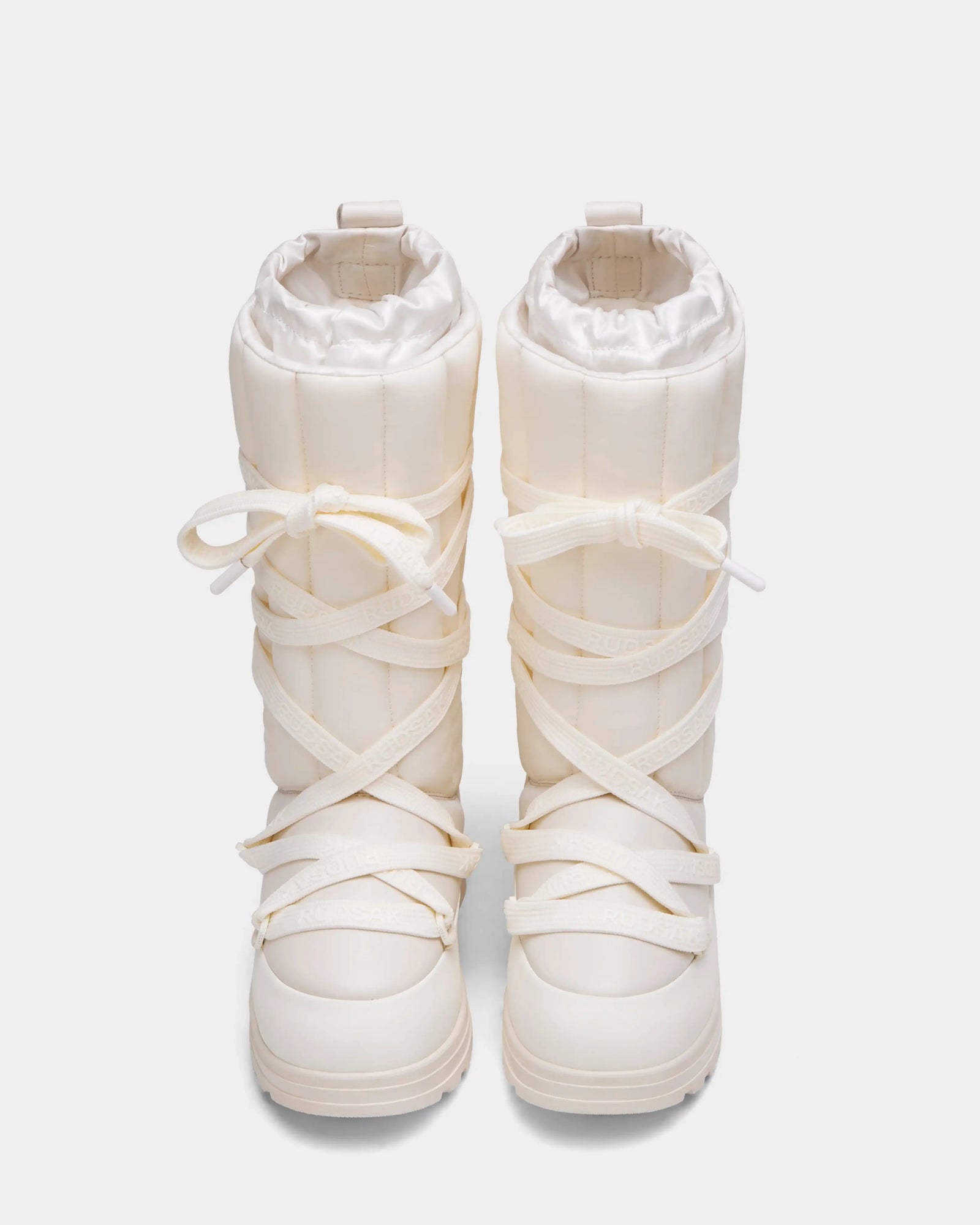 A pair of Rudsak RODIN - 8224502 Iceland womens tall white winter boots with thick padded uppers, chunky anti-slip soles, and crisscrossing white laces tied in bows, shown from above on a plain background.