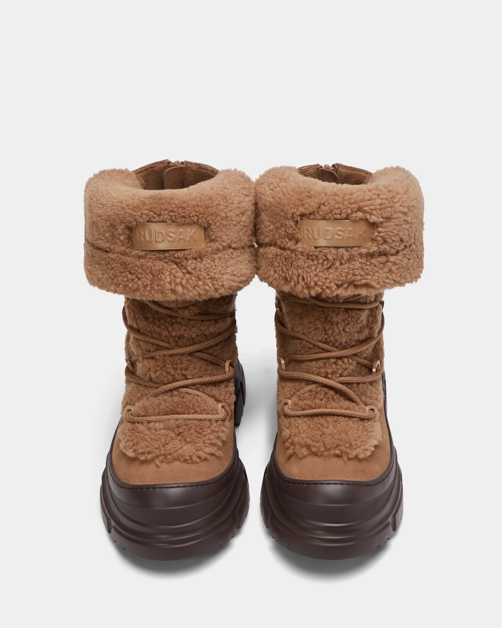 The ROKI - 8224533 Camel by Rudsak are womens winter ankle boots in brown faux shearling with chunky dark brown soles, front laces, folded cuffs, and the Rudsak logo on the cuff.