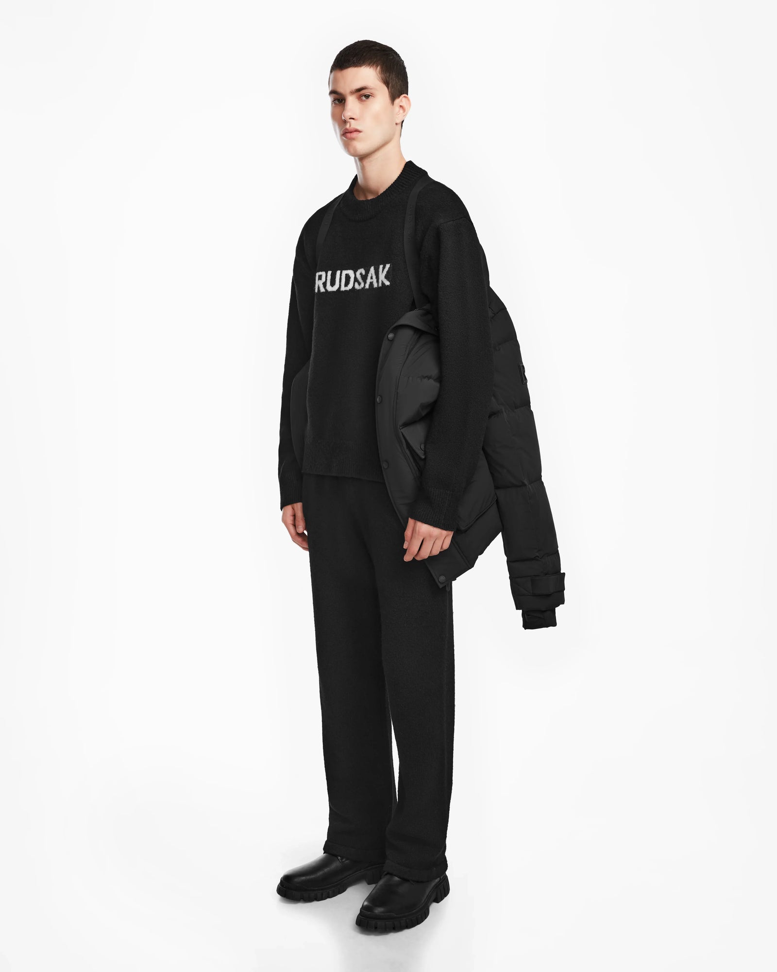 A man in black clothes wears the Rudsak ROKO - 6124510 Black mens quilted down parka, perfect for winter with cozy RDS-certified down insulation.