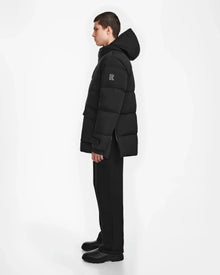 A person stands in profile wearing the Rudsak ROKO - 6124510 Black winter parka with RDS-certified down, paired with black pants and boots, set against a plain white background.