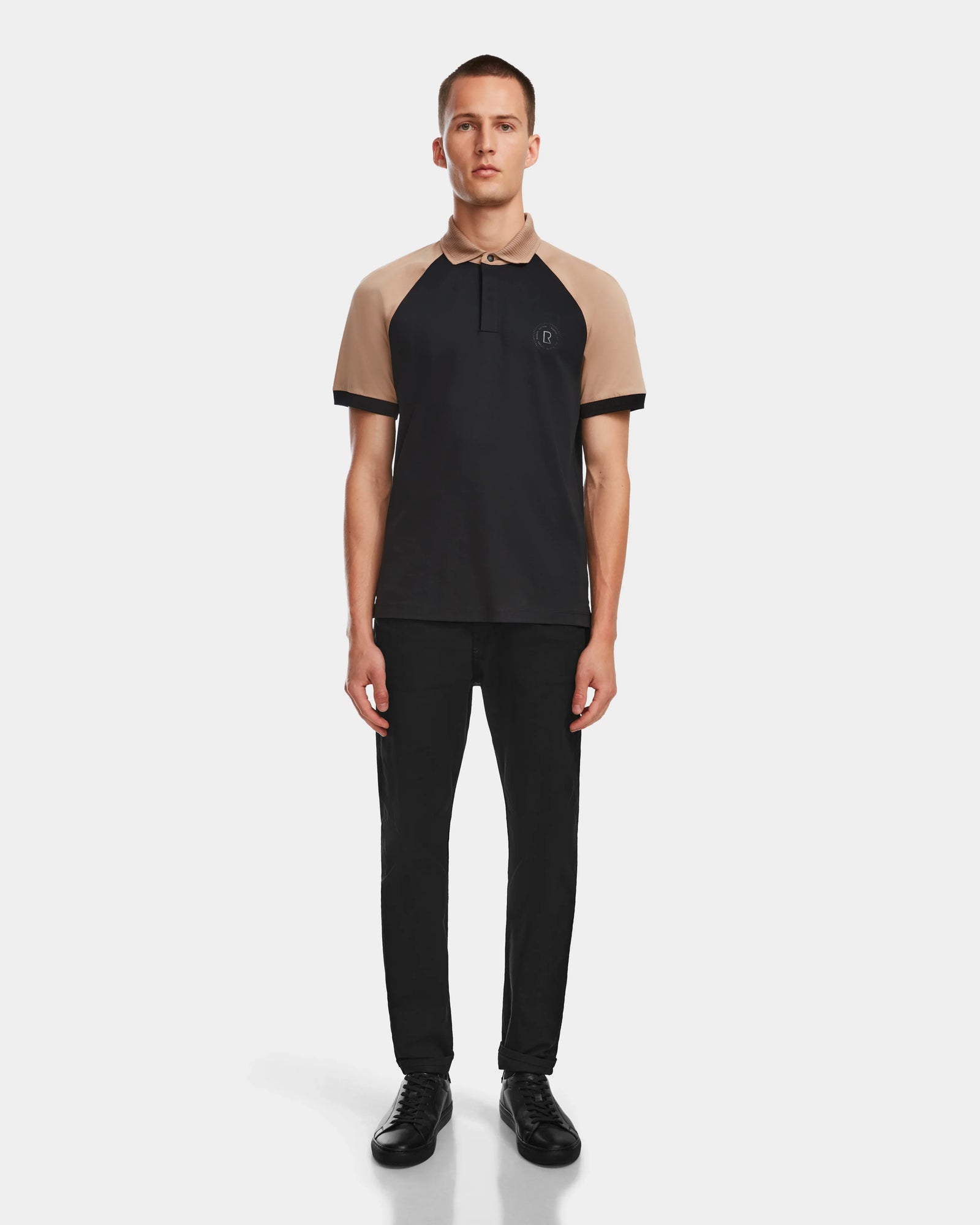 A man faces forward wearing the Rudsak WALTER - 6524531 Black/Camel premium cotton short sleeve polo, paired with black pants and shoes, set against a plain light background.