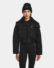 A woman models Rudsaks YVETTE - 8124710 Black women’s crop down puffer jacket with large buttons, paired with a black beanie and leggings, standing against a plain white background.