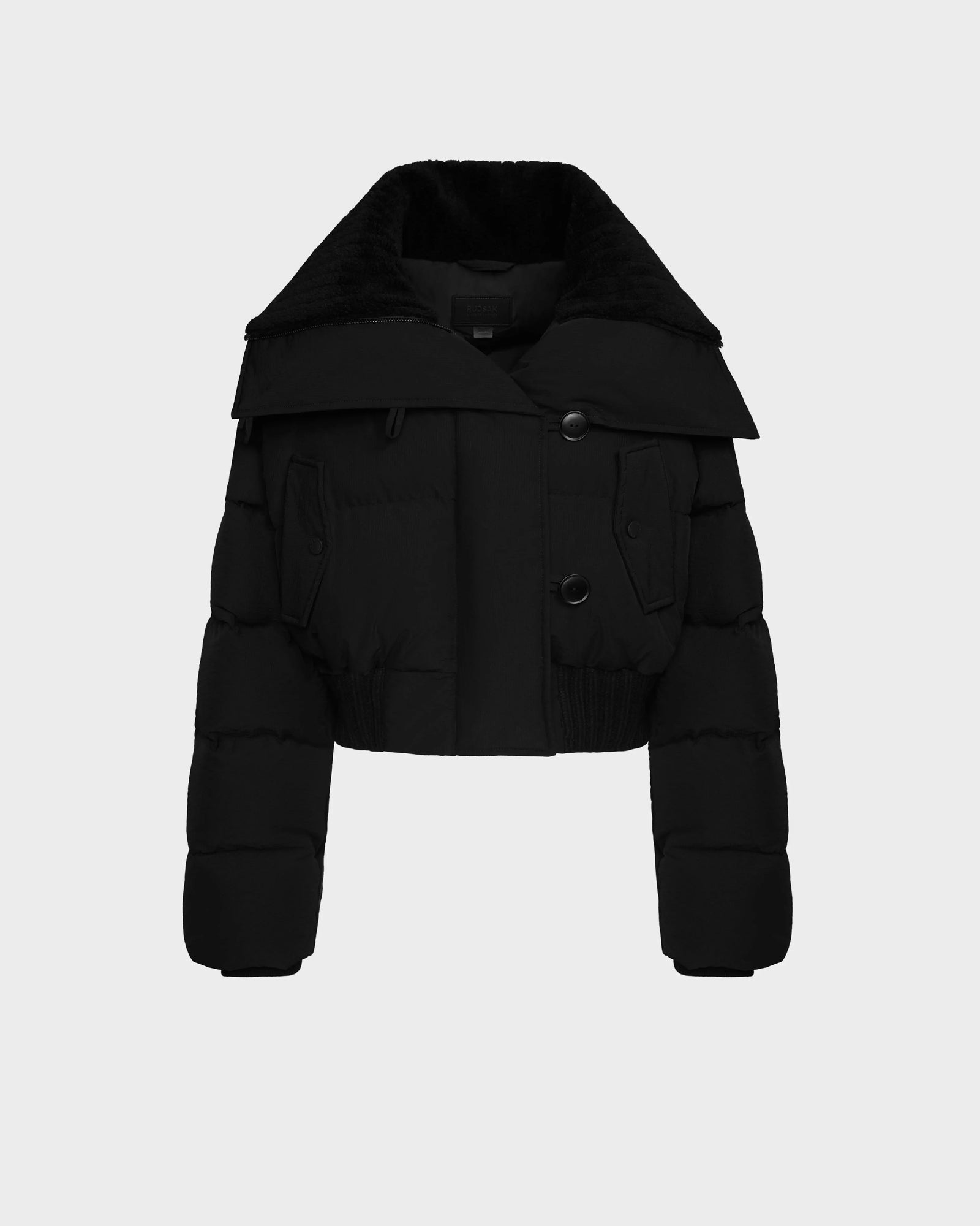 The Rudsak YVETTE - 8124710 Black is a chic women’s cropped puffer jacket with a large collar, two front buttons, flap chest pockets, and an elastic hem—perfect for stylish winter looks. Displayed on a plain light background.