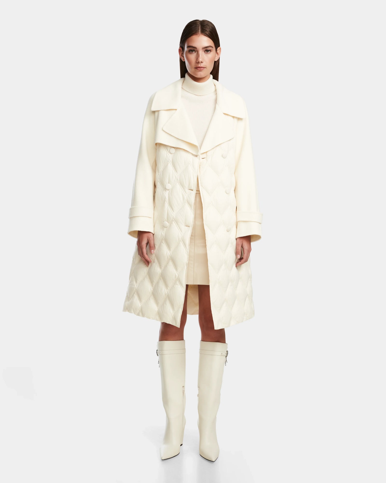 A woman faces forward, wearing the Rudsak ZOE - 8124711 Iceland white quilted down trench over a white turtleneck top, matching skirt, and knee-high boots against a plain light background.