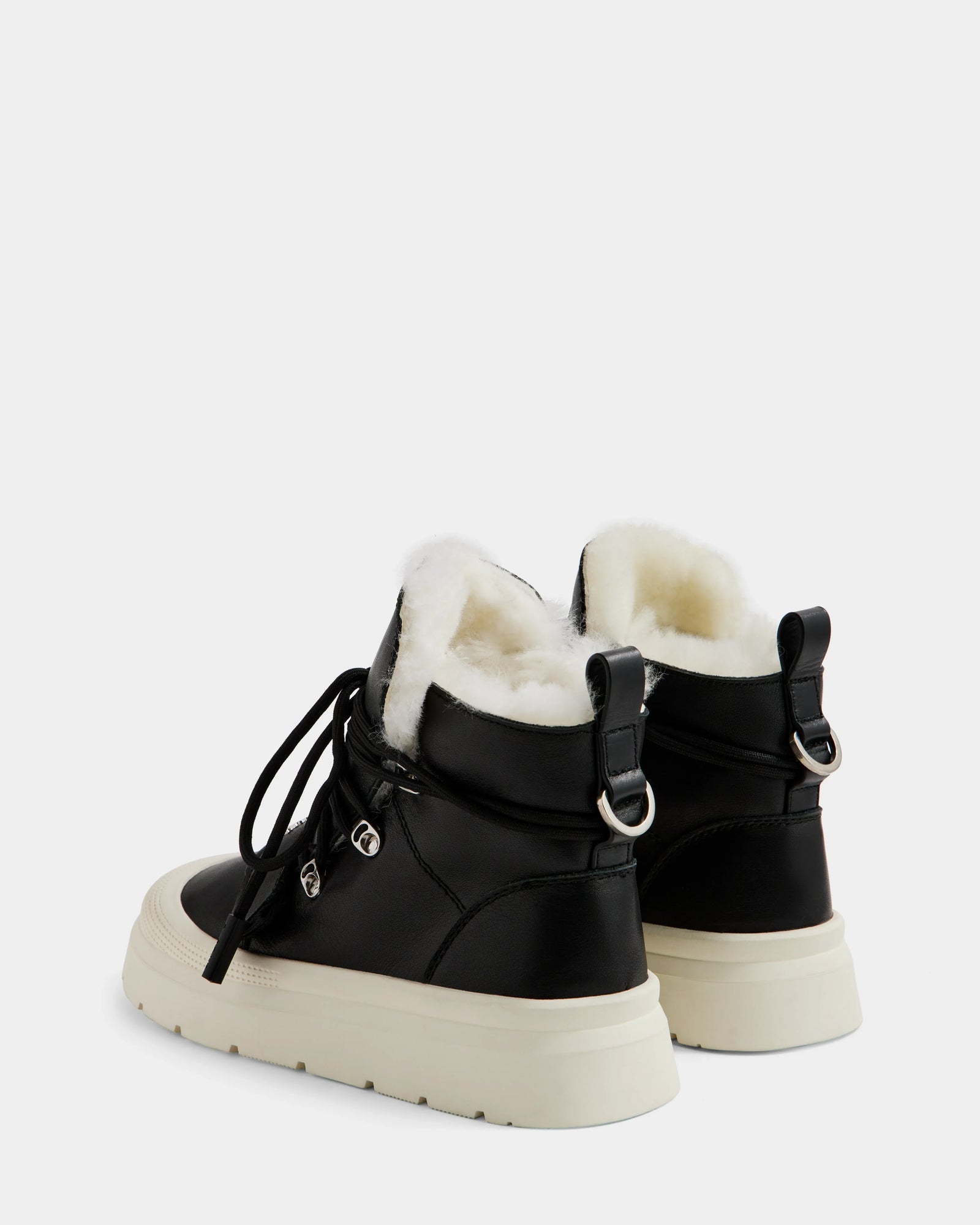 ALEXEY L - L225518 Black by Rudsak: black women’s leather winter boots featuring white wool lining, thick white soles, lace-up fronts, and silver hardware, shown from a back three-quarter angle against a plain light background.