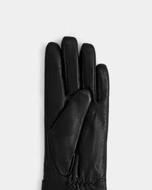 The Rudsak ALEXIA - L425543 Black women’s leather glove is displayed palm-up with the thumb across the palm against a light gray background—an elegant cold-weather accessory.