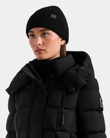 A person wearing the ANDREY - U425507 Black puffer jacket with a hood by Rudsak and a black rib-knit beanie, looking slightly to the side against a plain light background.