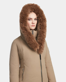 A woman models the Rudsak AURORE - L123561 Sand fitted winter coat with a large, fluffy brown fur-lined hood, looking directly at the camera against a plain white background.