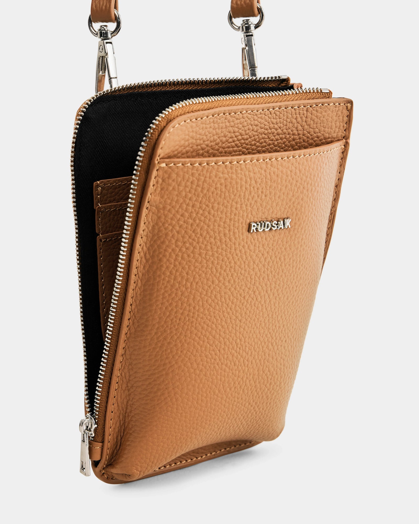 The Rudsak CELYN - L325514 Taupe is a women’s tan leather crossbody city bag with pebbled leather, silver zippers, a front pocket, and metal RUDSAK letters, shown open to reveal its organized interior compartments.