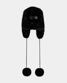 The Rudsak DEMI - L425539 Black women’s faux-fur aviator hat features ear flaps and long pom-pom strings, shown on a plain light gray background—ideal for combining stylish warmth in winter.