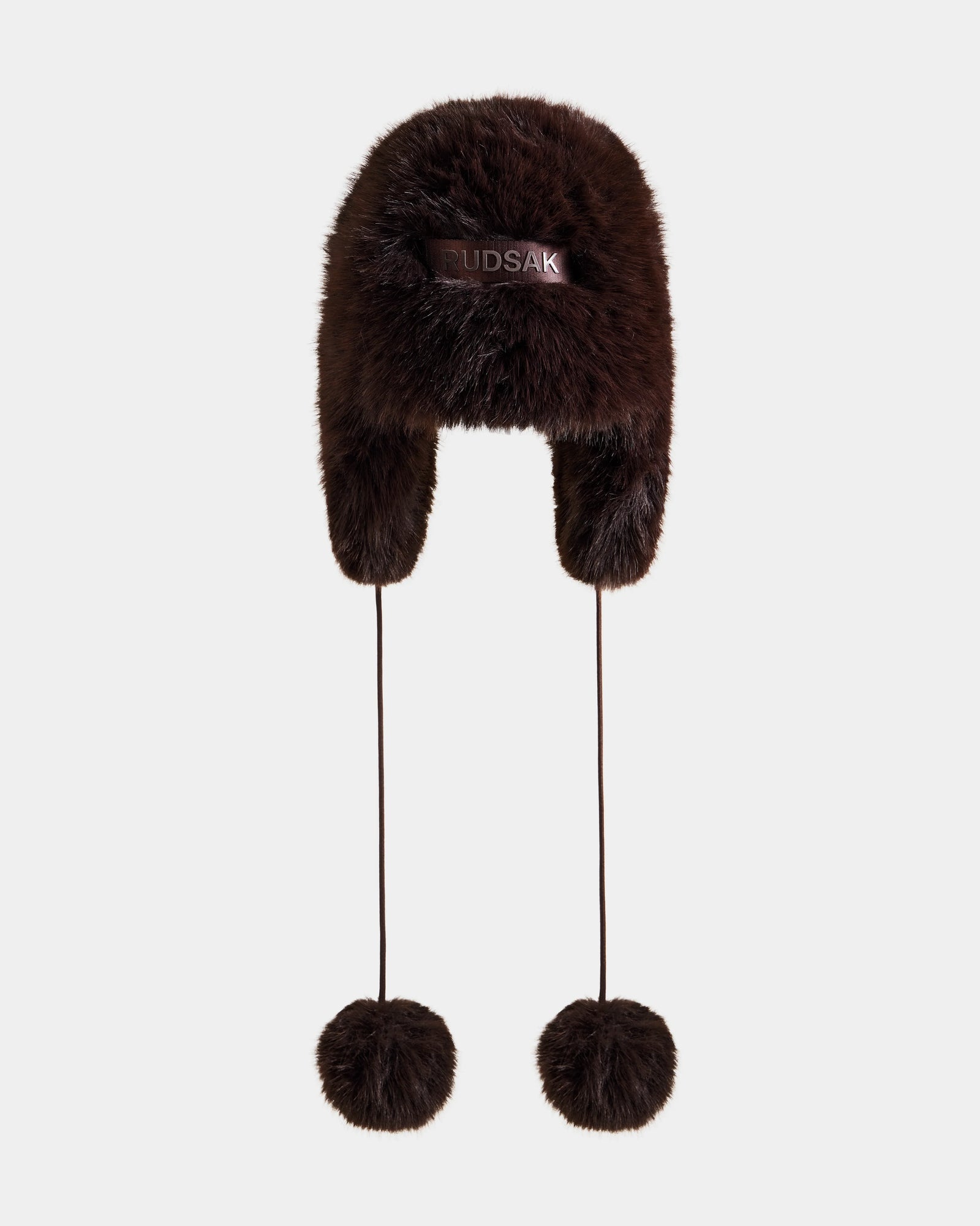 Stay cozy and stylish this winter with the DEMI - L425539 Espresso, a fluffy brown women's faux-fur aviator hat by Rudsak featuring ear flaps, long strings with fur pom-poms, and the Rudsak logo on the front.