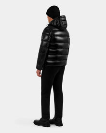 A person wearing the Rudsak DEMIAN S-R - M123505 Black puffer jacket, black beanie, pants, and boots stands facing away from the camera against a plain white background.
