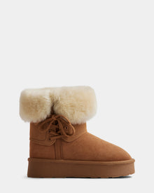The Rudsak INESA - L225026 Tan ankle boot features a tan suede exterior, flat sole, lace-up front, and thick cream fur cuff—ideal cozy winter footwear. Shown in profile on a white background.
