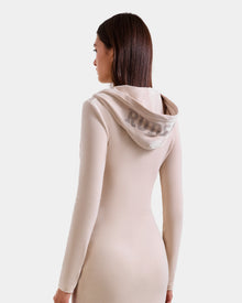 A woman with straight brown hair models the Rudsak ISABELLA - L525502 Cream, a fitted, long-sleeve beige velour hooded midi dress. 