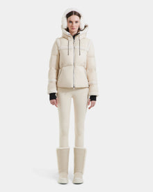 A woman stands facing forward against a plain white background wearing the Rudsak JULIANA - L124509 Vanilla women’s short down puffer with a hood, perfect for any winter wardrobe.