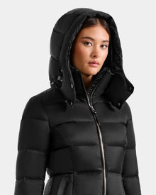 A woman in the Rudsak KATIA - L125564 black weather-resistant quilted puffer jacket, hood up, glances to the side against a plain light background.