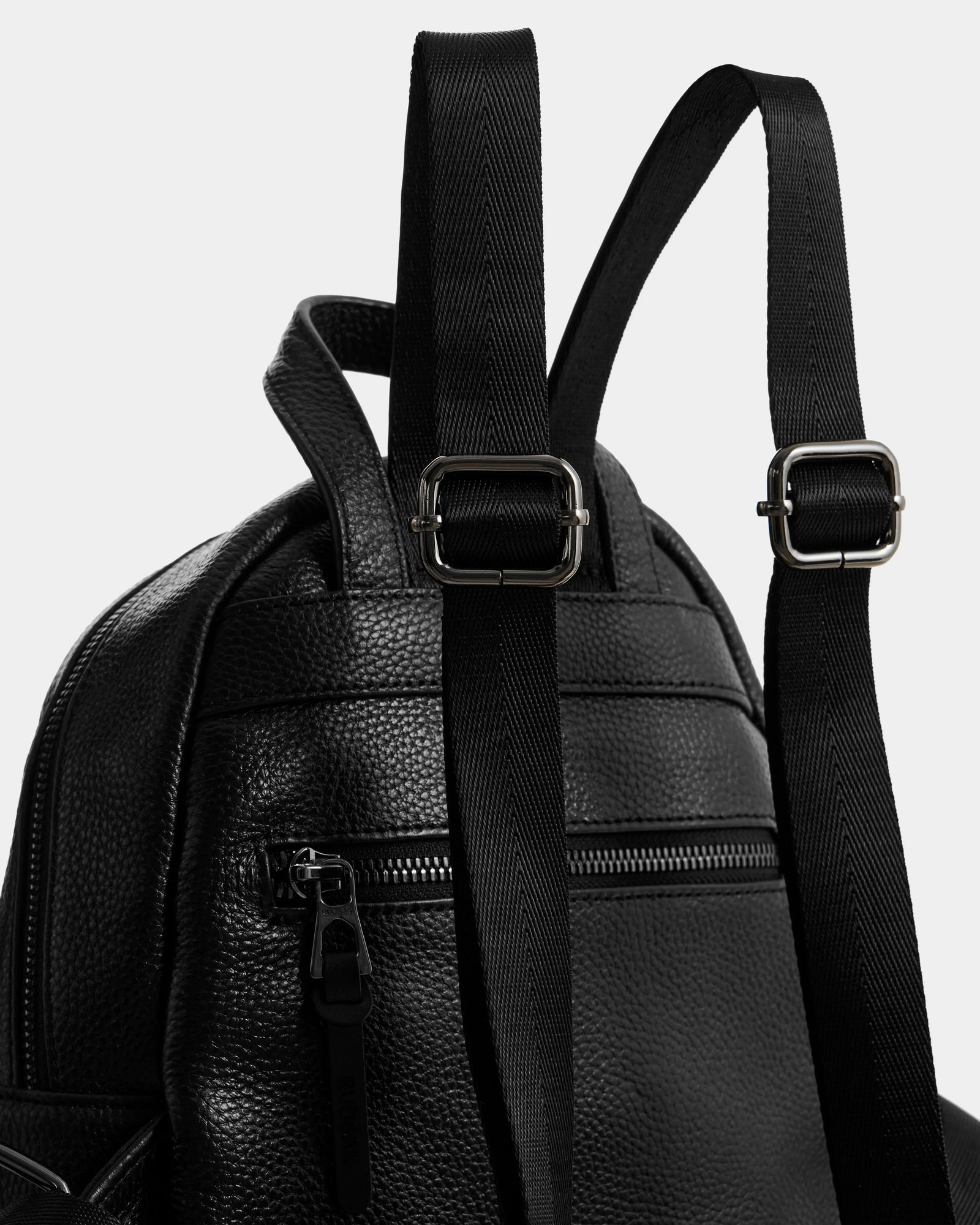 Close-up of the Rudsak KATTY - L325014 Black women’s mini backpack in black pebbled leather, featuring adjustable shoulder straps, metal buckles, a zippered front pocket, and textured material.