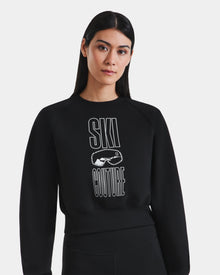 A woman with long dark hair wears the Rudsak LIDDIE - L525505 black cropped crewneck sweatshirt, featuring 