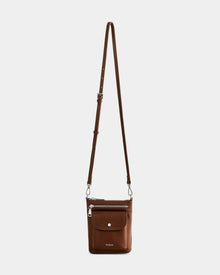 The Rudsak LILA - L325513 Mocha is a women’s crossbody bag in pebbled leather, featuring an adjustable strap, front flap pocket with snap closure, zippered main compartment, and a subtle embossed brand name at the bottom.