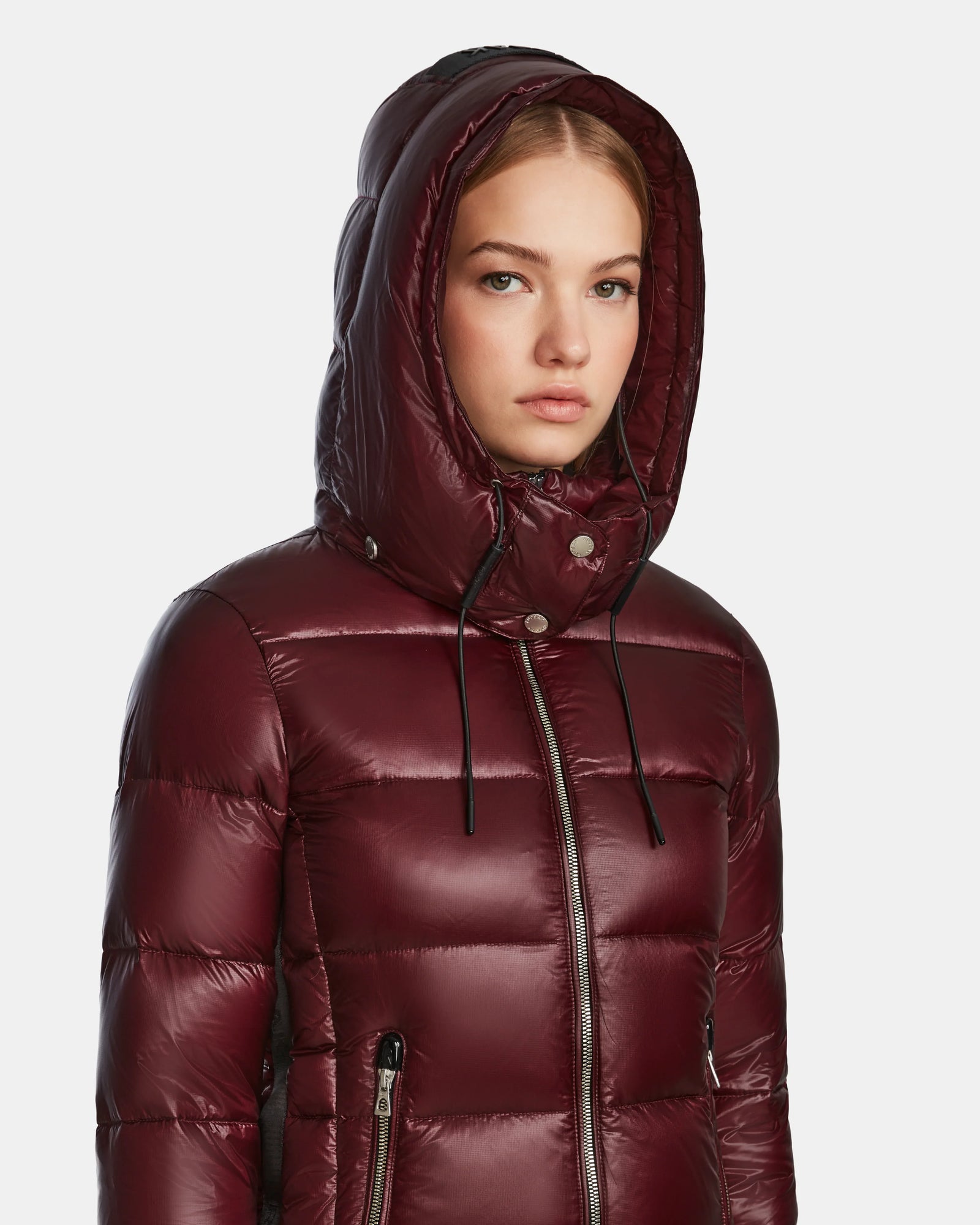 A young woman wears the Rudsak MIRRY S - L123545 winter coat in Wine with the hood up, looking ahead with a neutral expression against a plain light background.