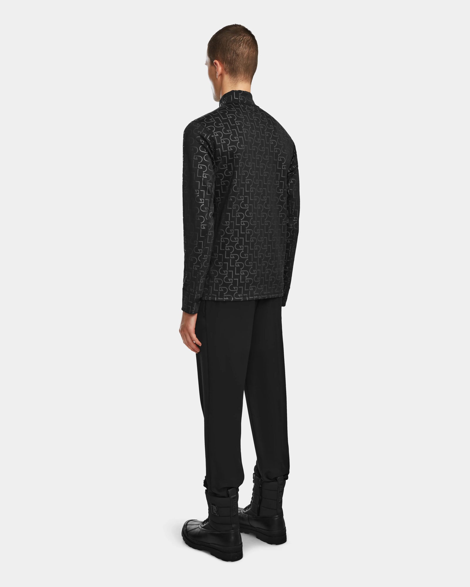 A person faces away, wearing the Rudsak ROMEO - 6524525 Black mock neck zip-up jacket with matching black pants and boots, set against a plain light gray background.