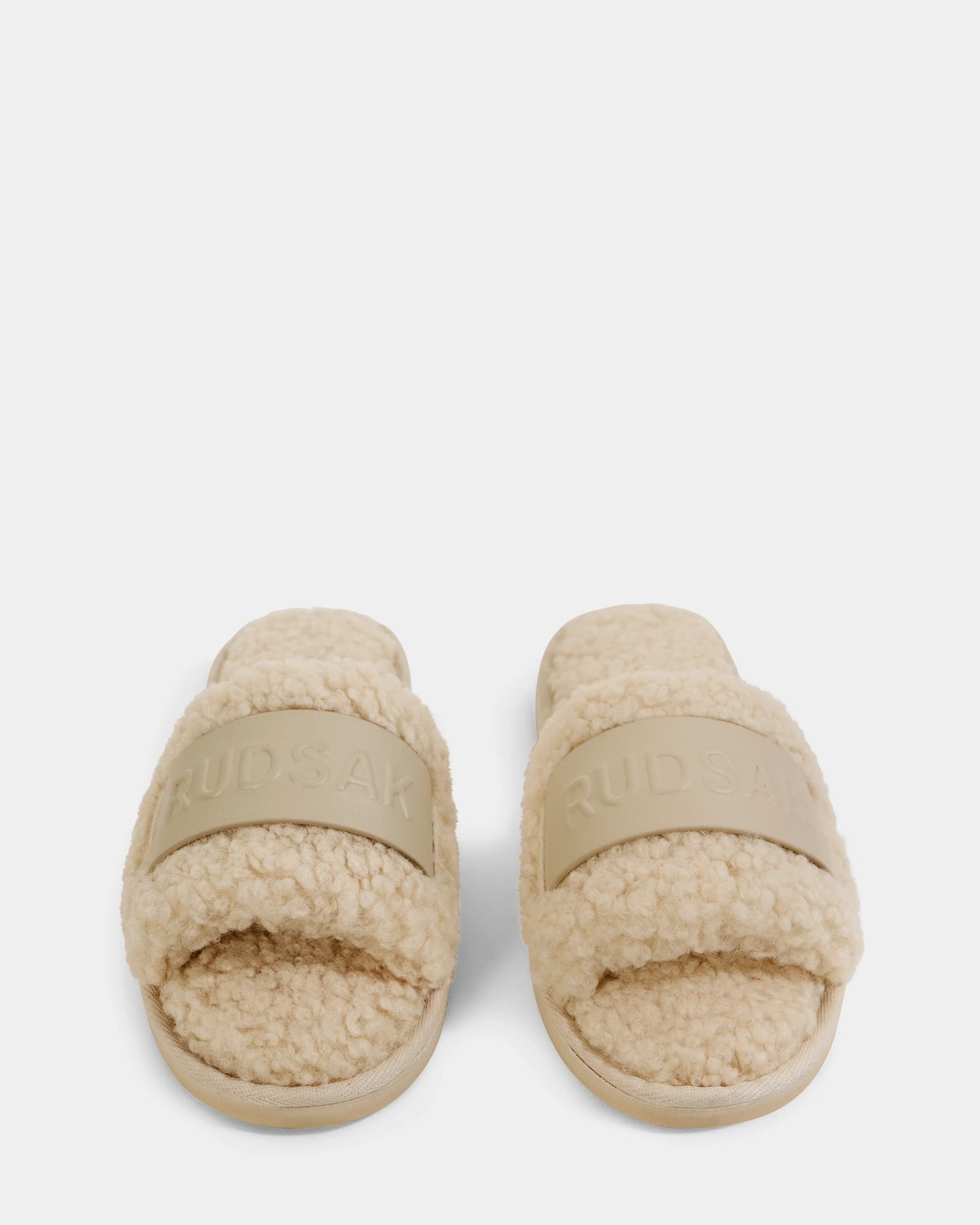 A pair of Rudsak TEDDY - L225517 Vanilla women’s faux-shearling slippers with thick, textured beige straps embossed with the brand name—perfect for upgrading your loungewear, shown on a white background.