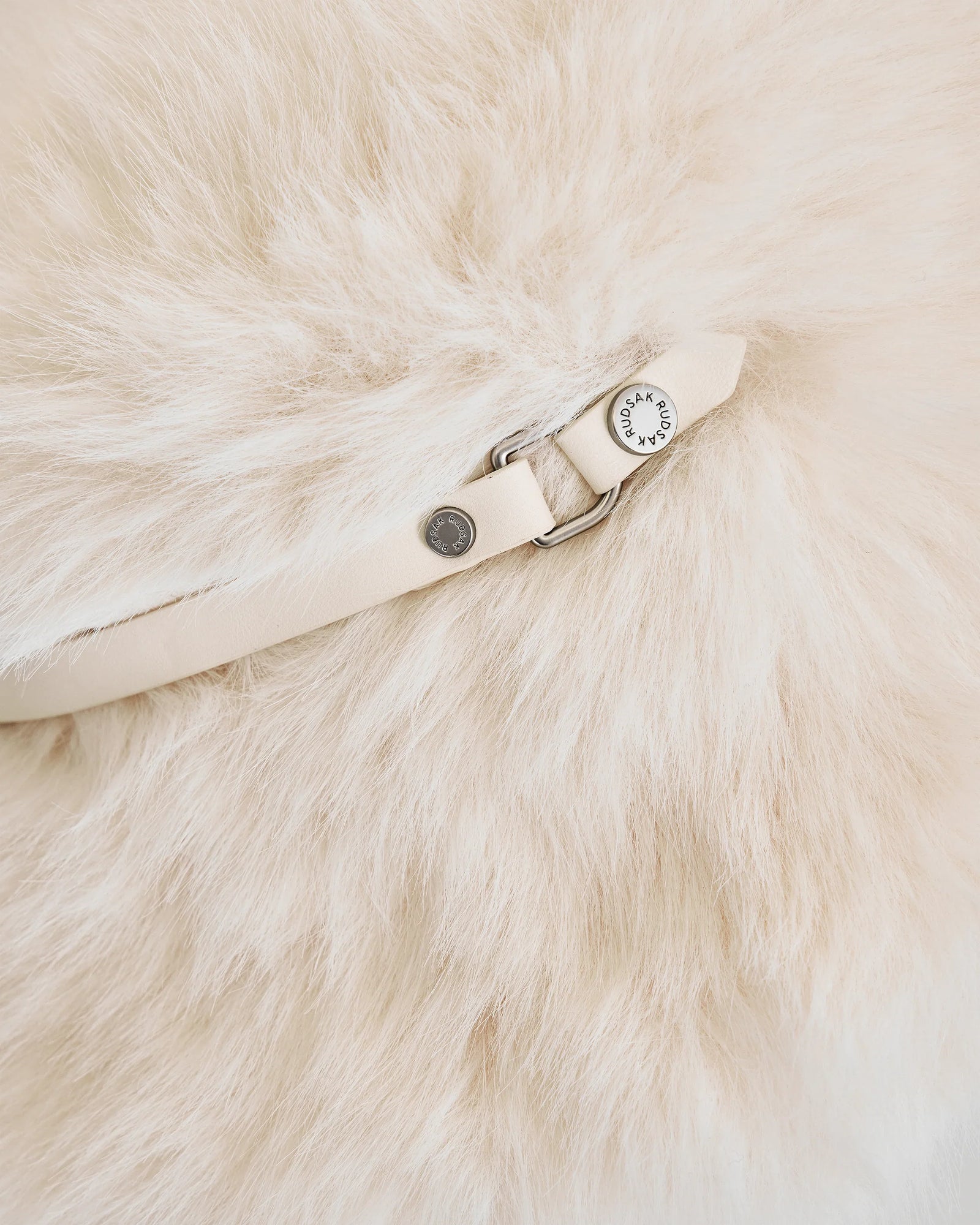 Close-up of the YURI - L425538 Iceland by Rudsak: a soft, cream-colored faux-fur bucket hat with pale vegan-leather trim, silver hardware, and a round metal tag—a chic women’s winter accessory.