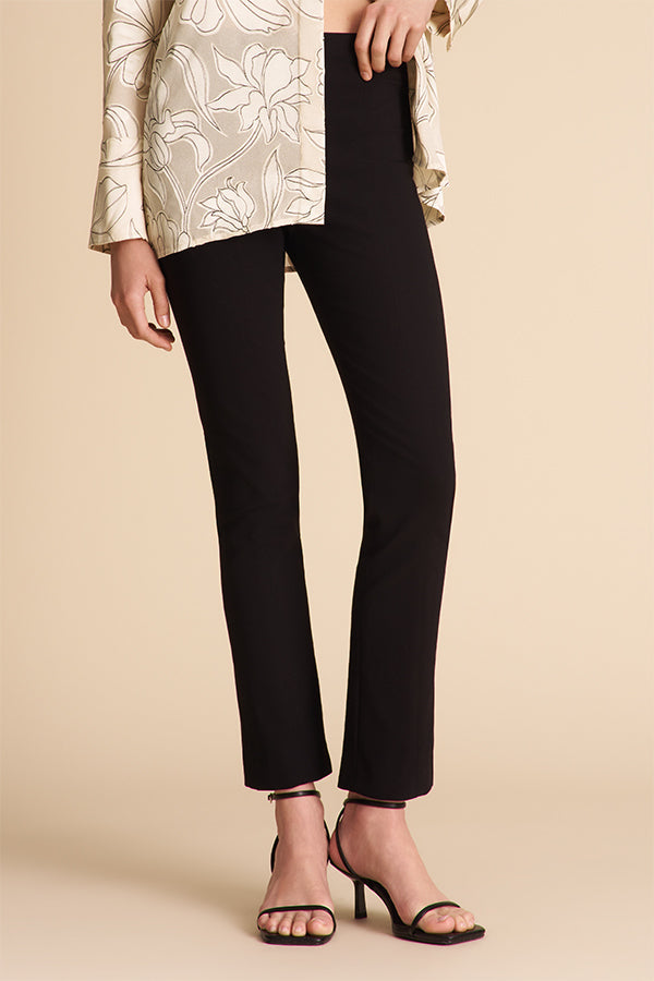Person wearing black pants and a patterned top on a beige background | Exclude