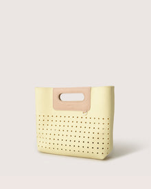The Graf Lantz Asobi Bag, a minimalist handbag made from Merino wool, showcases a cream design with perforated holes and a tan leather handle cutout, elegantly set against a plain white background.