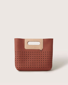 Introducing Graf Lantzs Asobi Bag: a sleek, minimalist brown handbag with a cutout handle. It features a beige accent at the top, small perforated holes in a grid pattern on the lower half, and an off-white backdrop, offering stylish simplicity.