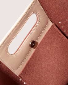 Close-up of an open Graf Lantz Asobi Bag in brown and beige leather, showcasing a rectangular cutout handle and button closure. Inside, a pocket with beige stitching contrasts beautifully with the textured lining. The minimalist design brings elegance to this accessory.
