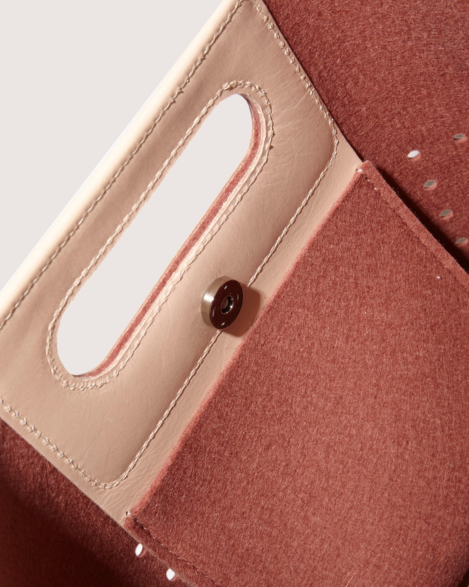 Close-up of an open Graf Lantz Asobi Bag in brown and beige leather, showcasing a rectangular cutout handle and button closure. Inside, a pocket with beige stitching contrasts beautifully with the textured lining. The minimalist design brings elegance to this accessory.