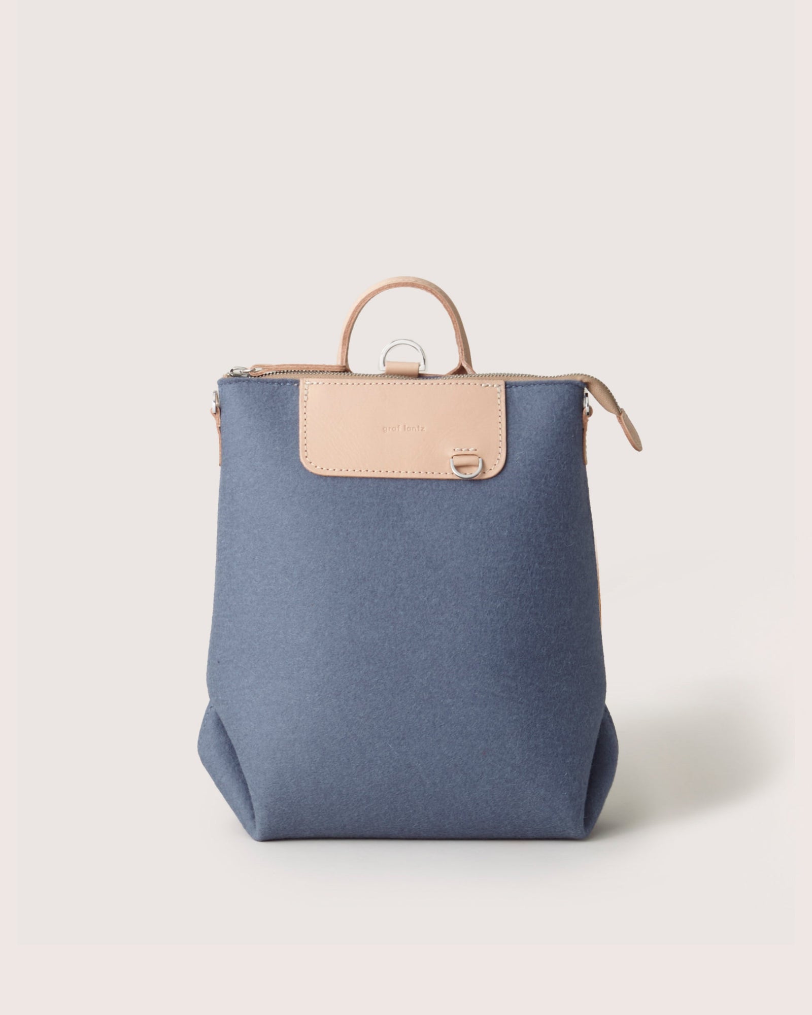 The Graf Lantz backpack, a chic and multifunctional piece, features a blue fabric body with light brown leather accents like a top handle and zipper. Positioned on a plain white background, it exemplifies commitment to sustainable fashion.