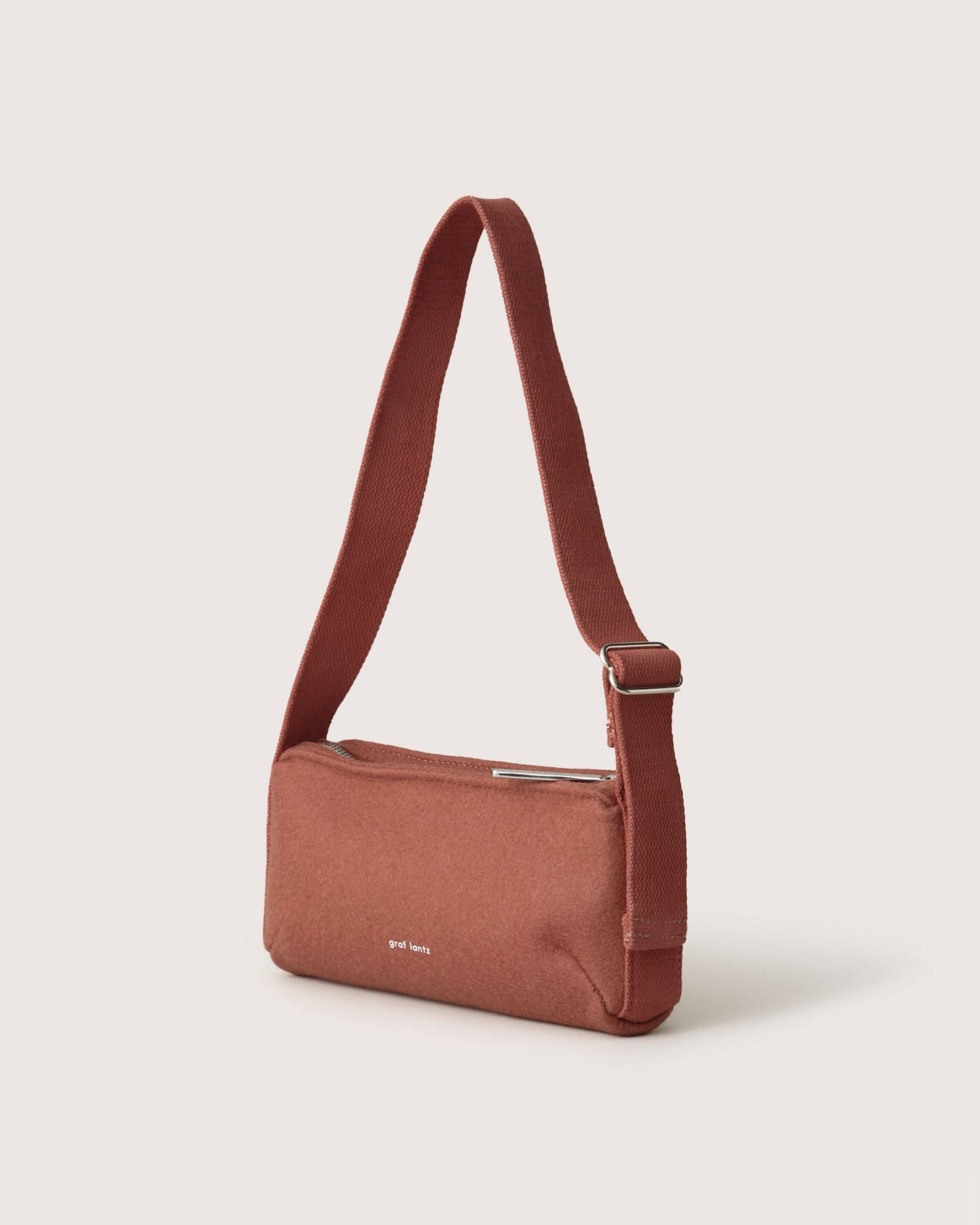 The Graf Lantz Campus Shoulder Bag, in rust Merino wool, features an adjustable strap and zippered compartment. Its simple rectangular design is enhanced by the subtle graf lantz branding on the side.
