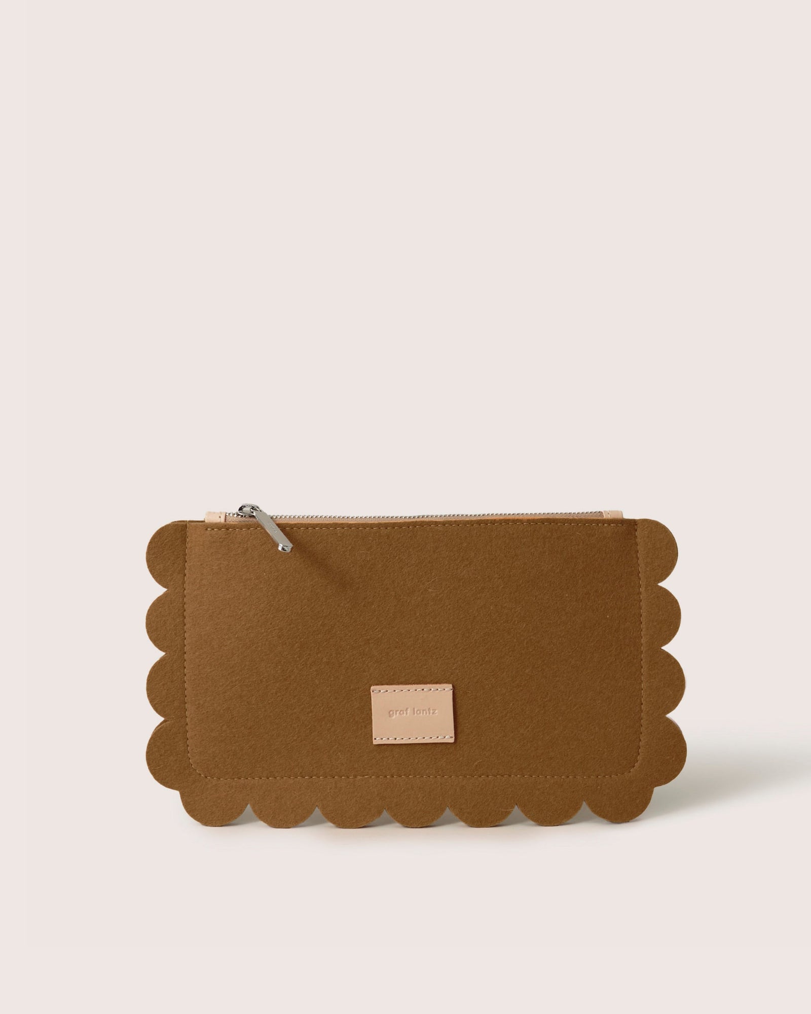 The Graf Lantz Deco Edge Pouch features scalloped edges, a zipper, and a small beige label on the front. Set against a plain white background, this versatile brown clutch adds elegance to any ensemble while securely storing essentials.