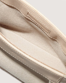 A close-up of a beige and cream open pouch, akin to the Frankie Merino Wool Clutch by Graf Lantz, showcases visible stitching. Its soft interior has a simple design without zippers or buttons, emphasizing texture and color contrast while promoting sustainable fashion.