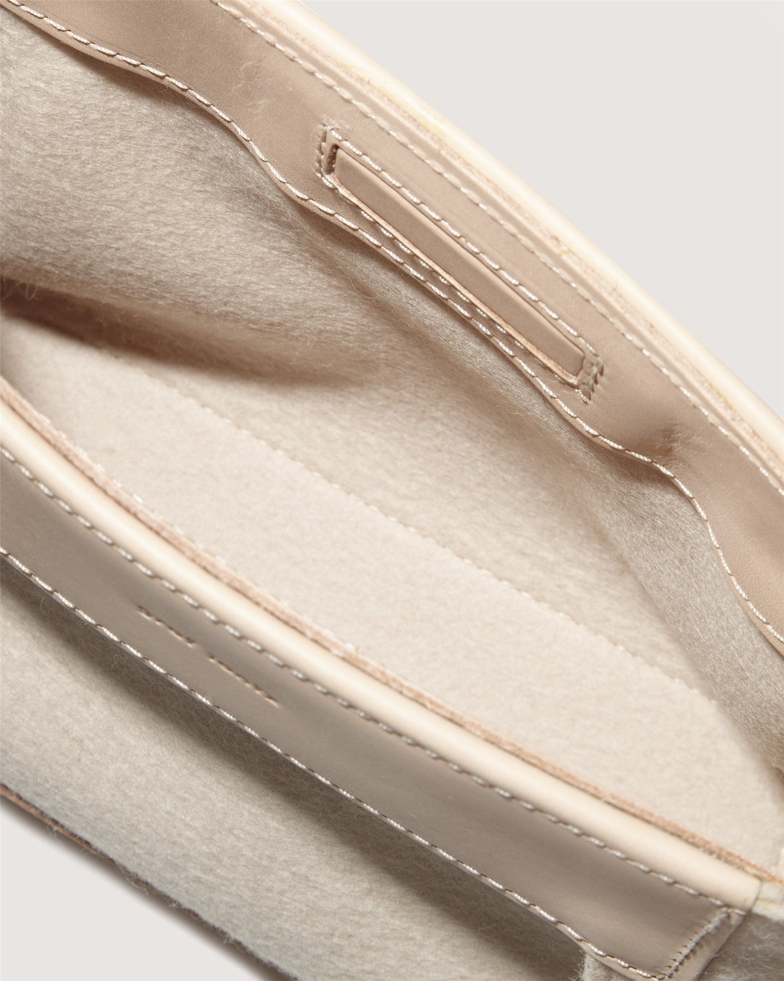 A close-up of a beige and cream open pouch, akin to the Frankie Merino Wool Clutch by Graf Lantz, showcases visible stitching. Its soft interior has a simple design without zippers or buttons, emphasizing texture and color contrast while promoting sustainable fashion.