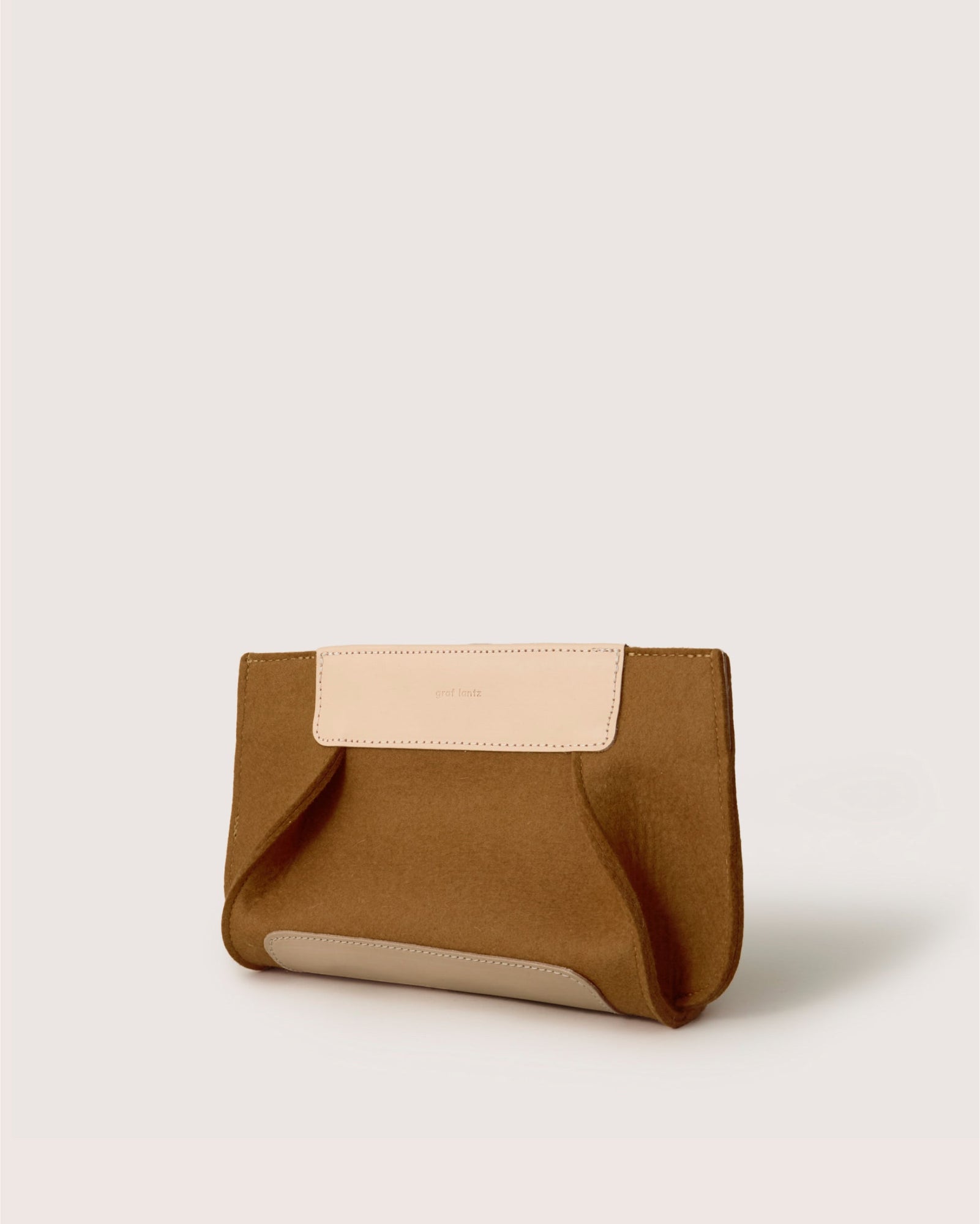 The Graf Lantz Frankie Merino Wool Clutch, in tan and light beige, is made from sustainable materials. With a minimalist design, flap closure, and embossed logo, it serves as an eco-friendly statement piece against a neutral backdrop for the modern minimalist.